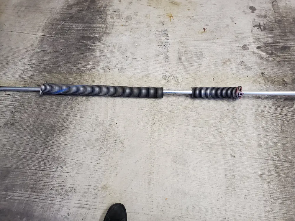A broken garage door torsion spring lying on a concrete floor